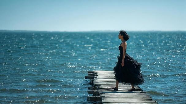海を背景に黒いドレスを着た女性 海を背景に黒いドレスを着た女性の写真