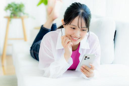 部屋でスマホを操作する若い女性 部屋でスマホを操作する若い女性の写真