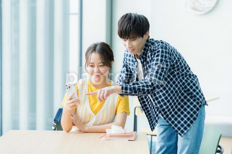スマホを見ながら話す学生たち スマホ,笑顔,大学生の写真素材
