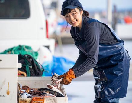 水揚げした魚介類を軽トラに積む漁師の女性の写真