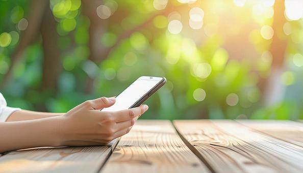 屋外のテーブルでスマホを持つ女性の手元 屋外のテーブルでスマホを持つ女性の手元の写真