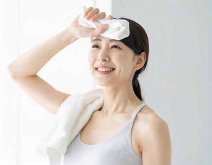 トレーニング後の汗を拭く笑顔の女性の写真