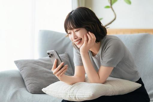 ソファに座ってスマホを使う笑顔の女性 ソファに座ってスマホを使う笑顔の女性 女性,スマホ,スマートフォンの写真素材