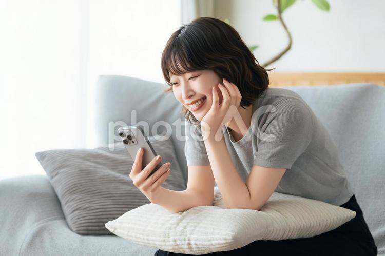 ソファに座ってスマホを使う笑顔の女性 女性,スマホ,スマートフォンの写真素材