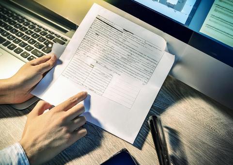 資料を手にパソコンを操作する 資料を手にパソコンを操作するの写真