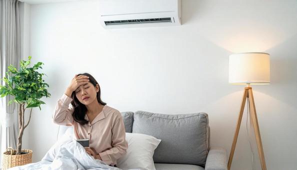 部屋のエアコンの下で寒がる女性 部屋のエアコンの下で寒がる女性の写真