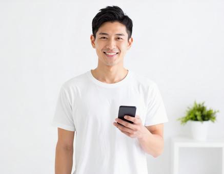 室内でスマホを持つ笑顔の白Tシャッツ男性 室内でスマホを持つ笑顔の白Tシャッツ男性の写真