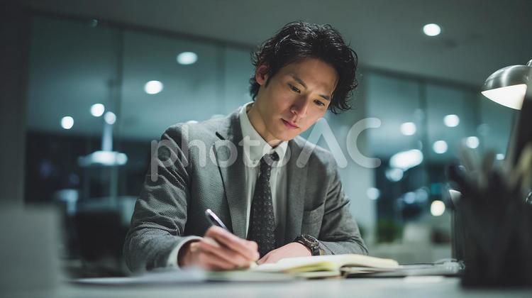デスクでメモを取る真剣な表情の日本人男性 ビジネス,スーツ,オフィスの写真素材