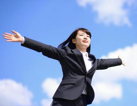 青空の中で笑顔で両手を広げるスーツの女性 青空の中で笑顔で両手を広げるスーツの女性の写真