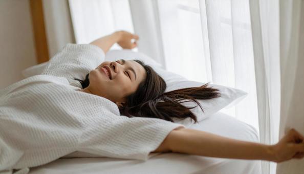 起床時に伸びをする白いパジャマの若い女性 起床時に伸びをする白いパジャマの若い女性の写真