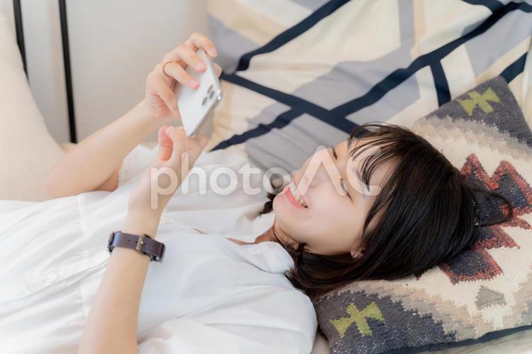 寝ながらスマホで動画を楽しむ女性 女性,スマホ,スマートフォンの写真素材