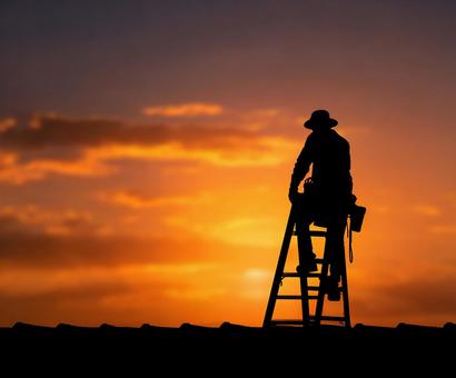 夕焼けを背景にした屋根職人のシルエット 夕焼けを背景にした屋根職人のシルエットの写真