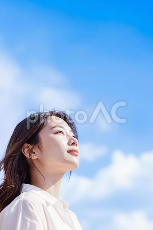 青空を背景にたたずむ女性（タテ） 青空,見上げる,女性の写真素材