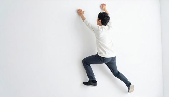 白い壁にのぼって乗り越える日本人男性 白い壁にのぼって乗り越える日本人男性の写真