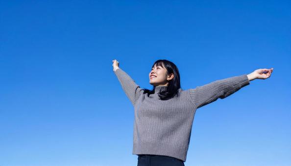 青空の下で伸びをする秋服の日本人女性 青空の下で伸びをする秋服の日本人女性の写真