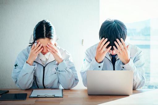 作業着を着た男女が頭を抱える 作業着を着た男女が頭を抱える 作業服,作業着,働く男女の写真素材