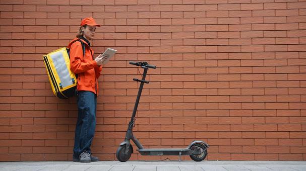 レンガ壁の前でタブレットを使うフードデリバリーの男性 配達,フードデリバリー,デリバリーの写真素材