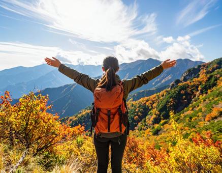 紅葉の山々を前に両手を広げる登山者 紅葉の山々を前に両手を広げる登山者の写真