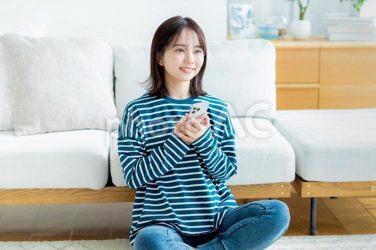 部屋でスマホを操作する若い女性 スマホ,若い女性,笑顔の写真素材
