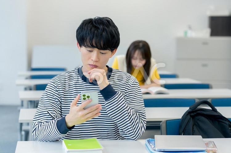 スマホを見ながら悩む大学生 スマホ,大学生,男性の写真素材
