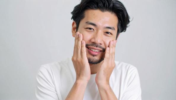両ほほを触って肌の潤いを実感する男性 両ほほを触って肌の潤いを実感する男性の写真