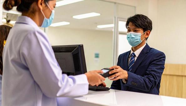 病院の会計窓口で会計をする男性患者 病院の会計窓口で会計をする男性患者の写真