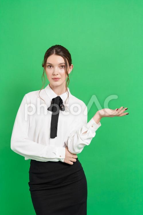 カメラ目線で案内する女性（緑背景） 女性,真顔,ジェスチャーの写真素材