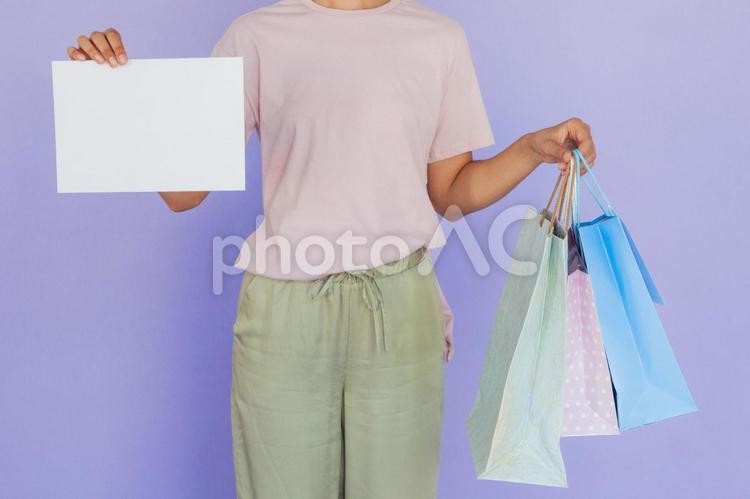 セールで買った物が入った紙袋を持って白い紙を見せている女性（顔なし） セール,ショップ,女性の写真素材