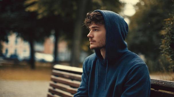 公園のベンチに座るパーカーの男性 公園のベンチに座るパーカーの男性の写真