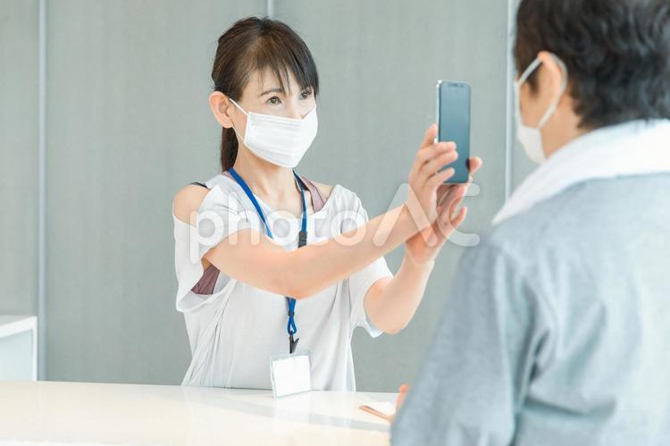 スポーツジムの受付をする女性（スマホ） 体温計,検温,スポーツジムの写真素材