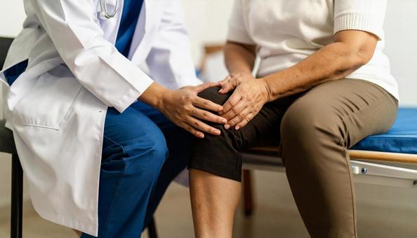 シニア女性の膝をマッサージする白衣の女性の写真