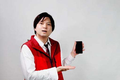 スマートフォンを紹介する男性 男性,スマートフォン,赤いベストの写真素材