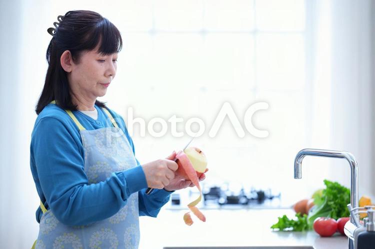 キッチンでりんごの皮をむく中年女性の横顔 主婦,家政婦,エプロンの写真素材