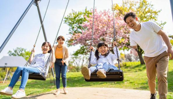 公園のブランコで遊ぶ日本人の家族 公園のブランコで遊ぶ日本人の家族の写真