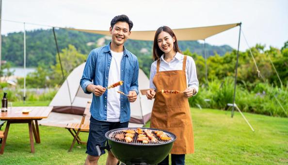 バーベキューで串を持って笑顔の男女 バーベキューで串を持って笑顔の男女の写真