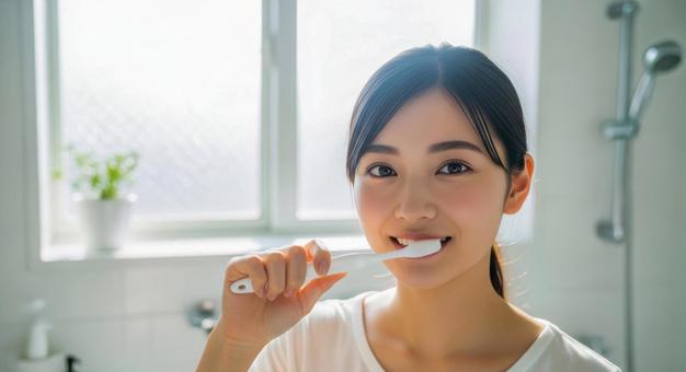 朝の洗面所で歯磨きをする若い女性 朝の洗面所で歯磨きをする若い女性の写真