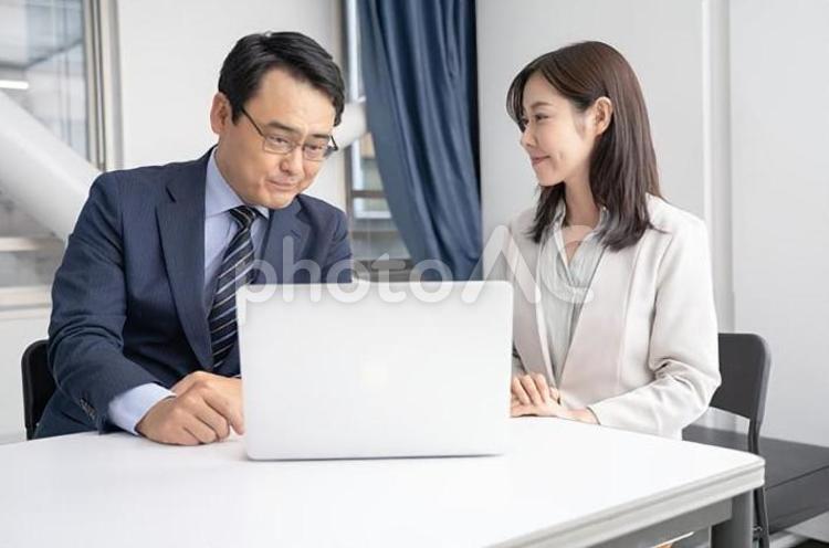 オフィスでノートパソコンを見ながら打ち合わせをする男女のビジネスマン 男性,女性,ビジネスの写真素材