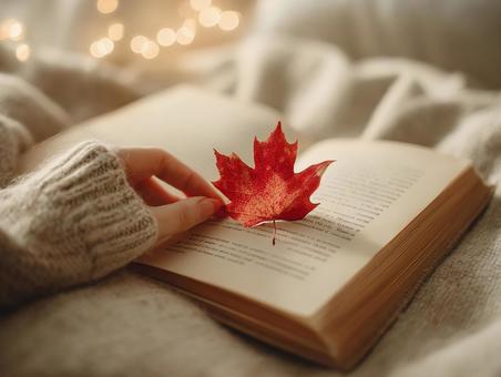 ニットと紅葉を挟んだ読書の手の写真