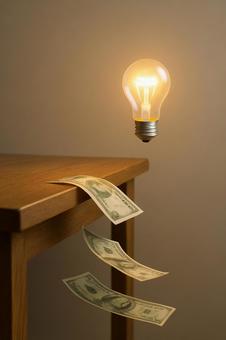 失われる資金(机から落ちる紙幣と電球) 失われる資金(机から落ちる紙幣と電球)の写真