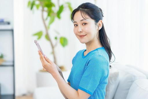 部屋でスマホを操作する女性 スマホ,笑顔,部屋の写真素材
