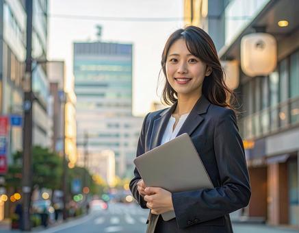 オフィス街でPCを持って微笑む女性社員 オフィス街でPCを持って微笑む女性社員の写真