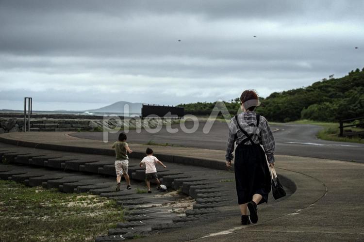 ＜素材＞梅雨の荒れた海辺を駆け回る親子 女性,子供,男性の写真素材