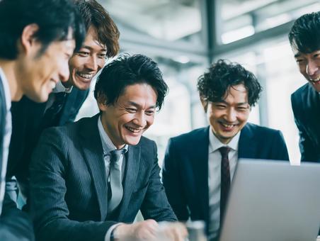 パソコンを囲んで話し合う男性社員たちの写真