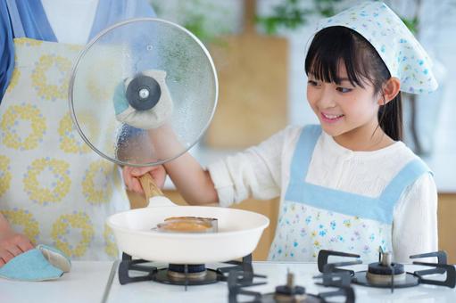 料理の仕上がりを楽しみにするエプロン姿の少女 女の子,笑顔,笑うの写真素材