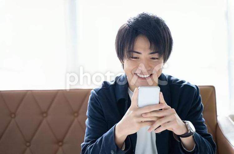 スマホを操作する20代男性 男性,スマートフォン,リビングの写真素材