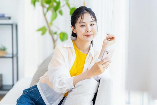 部屋でスマホを操作する女性 部屋でスマホを操作する女性 スマホ,笑顔,部屋の写真素材