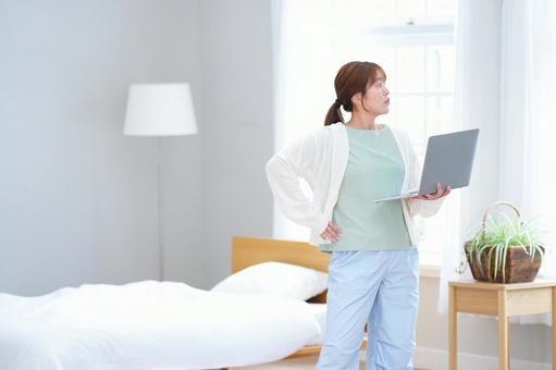 パソコンを持ち腰に手を当てポーズする女性の写真