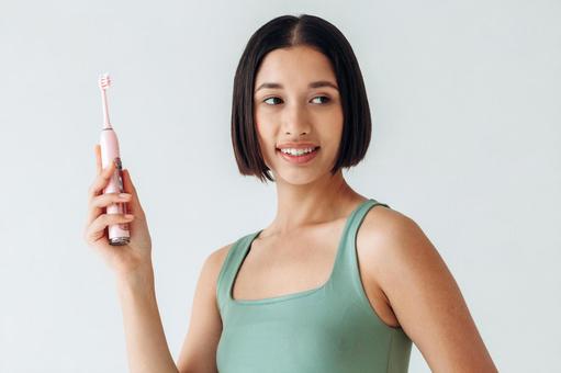 よそ見して電動歯ブラシを持つ女性 よそ見して電動歯ブラシを持つ女性の写真