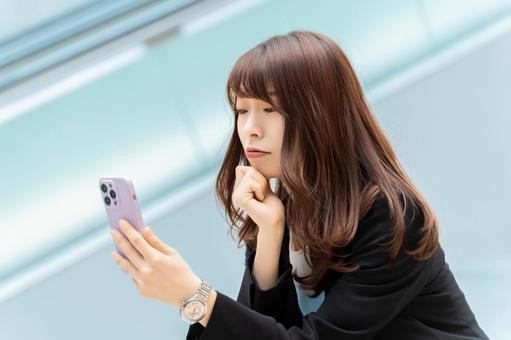 スマホを見て考える女性・ビジネスウーマン スマホを見て考える女性・ビジネスウーマンの写真