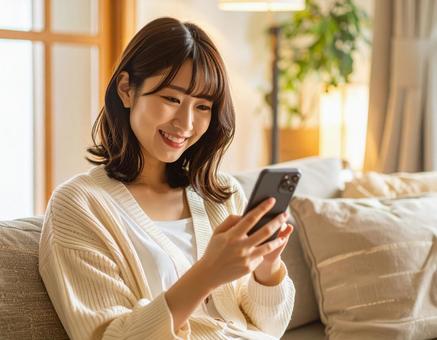 自宅のリビングでスマホを操作する女性の写真